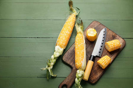 Board with fresh corn cobs and knife on color wooden backgroundの写真素材