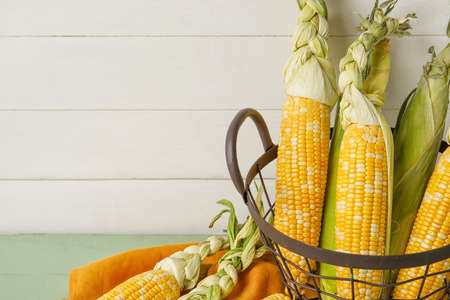 Basket with fresh corn cobs on light wooden backgroundの写真素材