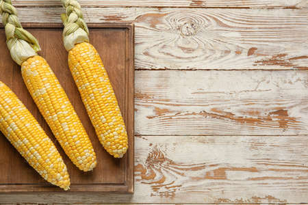 Board with fresh corn cobs on light wooden table