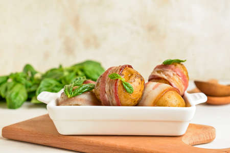 Baking dish of tasty baked potatoes with bacon on light backgroundの写真素材