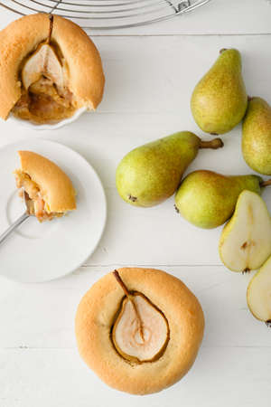 Tasty pear pot pies and fresh fruits on light wooden background