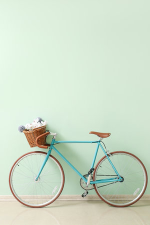 Stylish bicycle with wicker basket and flowers near green wallの写真素材