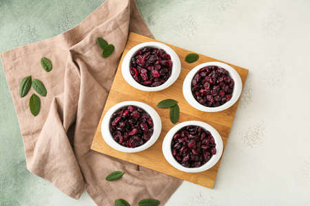 Bowls with tasty dried cranberries on light background