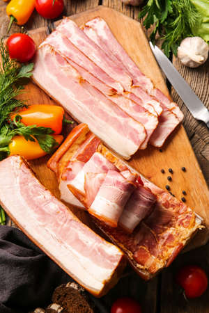 Board with tasty smoked bacon and fresh vegetables on wooden backgroundの写真素材