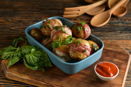 Baking dish of tasty baked potatoes with bacon on wooden backgroundの写真素材