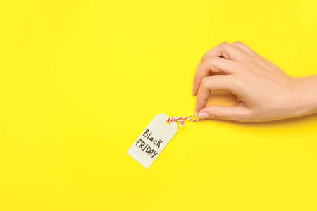 Female hand and tag with text BLACK FRIDAY on color backgroundの写真素材