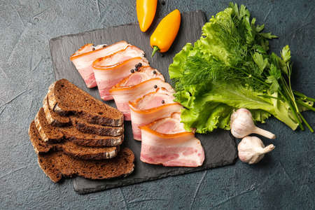 Composition with slices of tasty smoked bacon on dark background