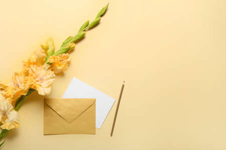 Beautiful gladiolus flowers with envelope, card and pencil on color backgroundの写真素材