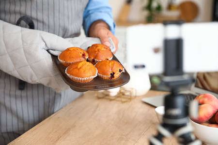 Handsome man with tasty peach muffins recording video in kitchenの写真素材