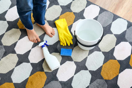 Female legs and cleaning supplies on colorful carpetの写真素材