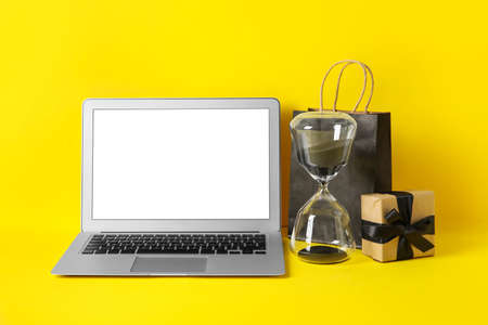 Laptop, hourglass, shopping bag and gift on color background. black friday sale