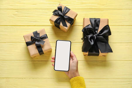 Hand with phone and gifts on wooden background. black friday sale