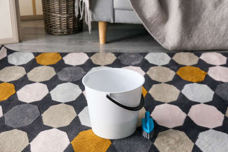 Bucket and cleaning brush on colorful carpet in roomの写真素材