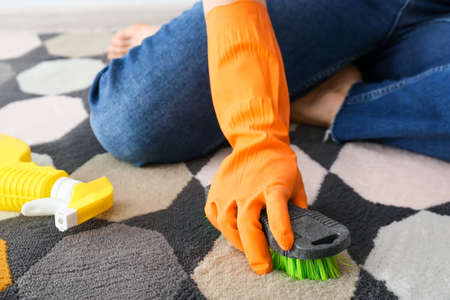 Housewife cleaning colorful carpet with brush at home, closeup