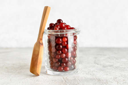 Jar with healthy cranberries on light background