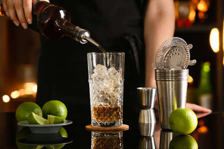 Female bartender making refreshing Long Island iced tea on table in bar