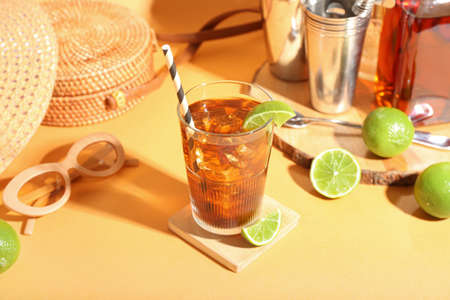 Glass of refreshing Long Island iced tea, limes and sunglasses on color backgroundの写真素材