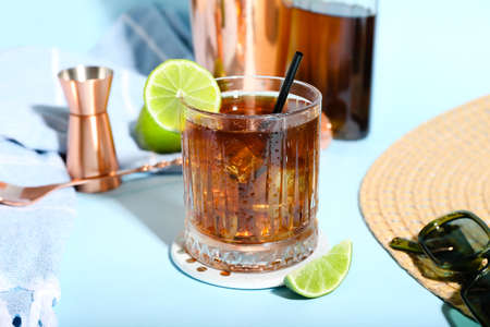 Glass of refreshing Long Island iced tea, lime and sunglasses on color background
