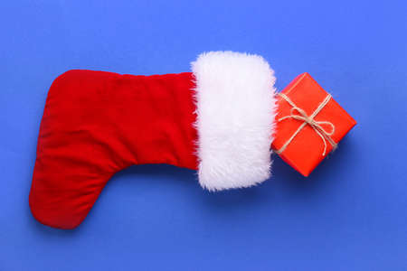 Gift box and Santa Claus stocking on color background