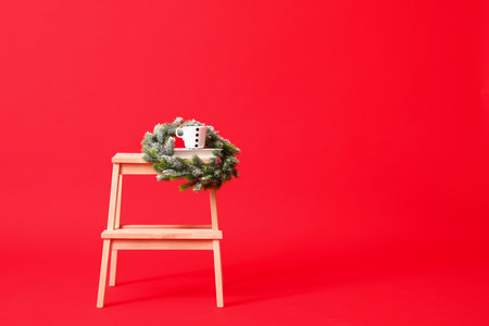 Wooden step stool with Christmas wreath and cup on red backgroundの写真素材