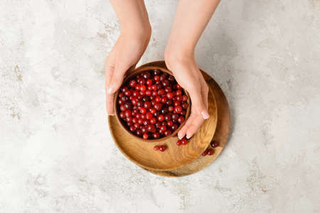 Woman holding bowl of ripe cranberry on light background, closeupの写真素材