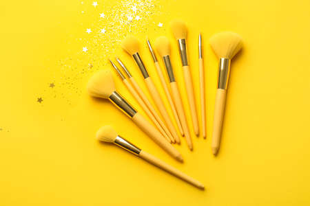 Set of stylish makeup brushes and confetti on yellow backgroundの写真素材