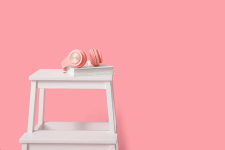 White step stool with headphones and books on pink background