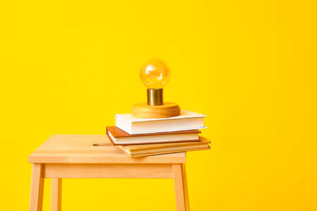 Wooden step stool with books and lamp on yellow background