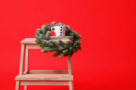 Wooden step stool with Christmas wreath and cup on red backgroundの写真素材