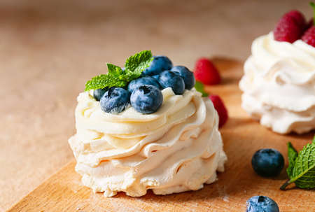 Wooden board of tasty Pavlova cakes with fresh berries on color background, closeup