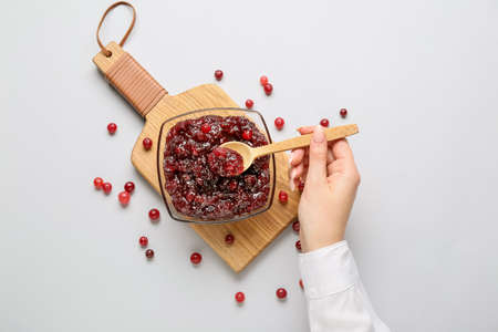 Woman eating tasty cranberry jam on light backgroundの写真素材