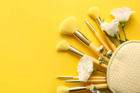 Cosmetic bag with stylish makeup brushes and flowers on yellow backgroundの写真素材