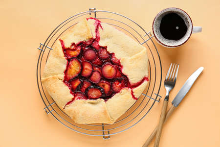 Grid with tasty plum galette and cup of coffee on color backgroundの写真素材