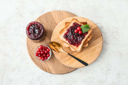 Wooden boards with toasts, cranberry jam and berries on light background