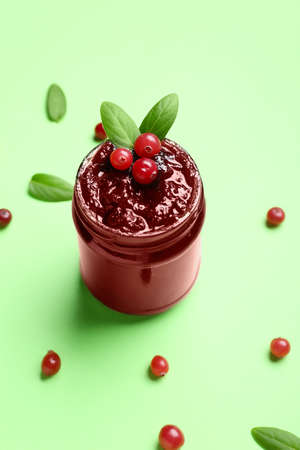 Glass jar with tasty cranberry jam on green backgroundの写真素材