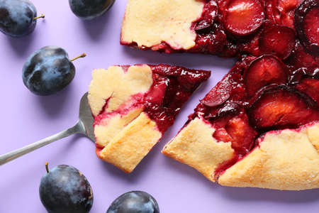Spatula with piece of fresh plum galette on purple background, closeup