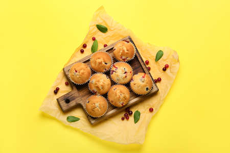 Wooden board with tasty cranberry muffins on color backgroundの写真素材