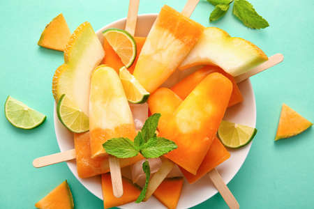Plate with tasty melon icicles on color background