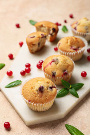 Board with delicious cranberry muffins on beige backgroundの写真素材