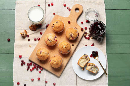Board with delicious cranberry muffins and glass of milk on green wooden backgroundの写真素材
