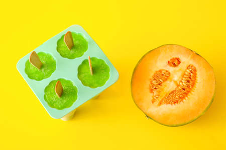 Containers with tasty popsicles and melon on yellow backgroundの写真素材