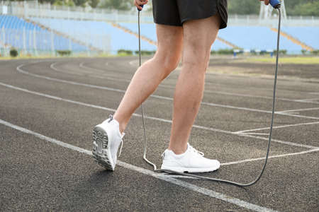 Legs of sporty young man with skipping rope at stadium