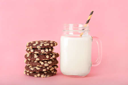 Tasty cookies with white chocolate chips and mason jar of milk on color background