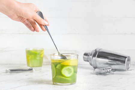 Female hand with spoon and glass of tasty lemonade on light background