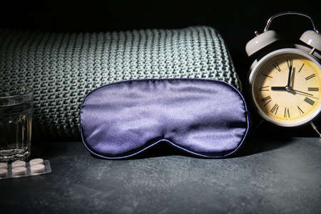 Sleep mask, alarm clock, glass of water and pills on dark backgroundの写真素材