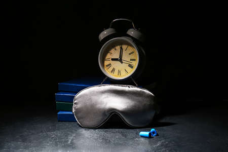 Sleep mask, alarm clock and earplugs on dark backgroundの写真素材