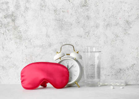 Sleep mask, alarm clock, glass of water and pills on light backgroundの写真素材