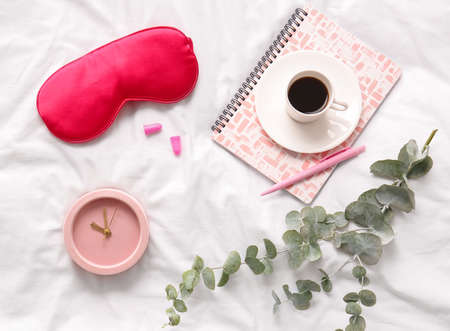 Sleep mask, alarm clock and cup of coffee on light fabric backgroundの写真素材
