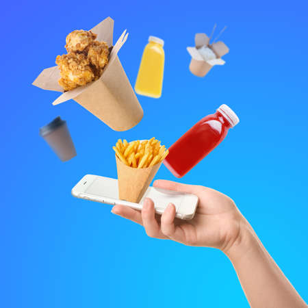 Human hand with smartphone and many tasty snacks on blue background. Concept of ordering foodの写真素材