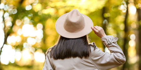 Pretty young woman wearing hat and coat while walking in autumn park, back viewの写真素材